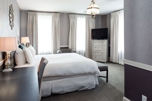 A hotel room with a large bed, a TV, a dresser, and a desk with a lamp.