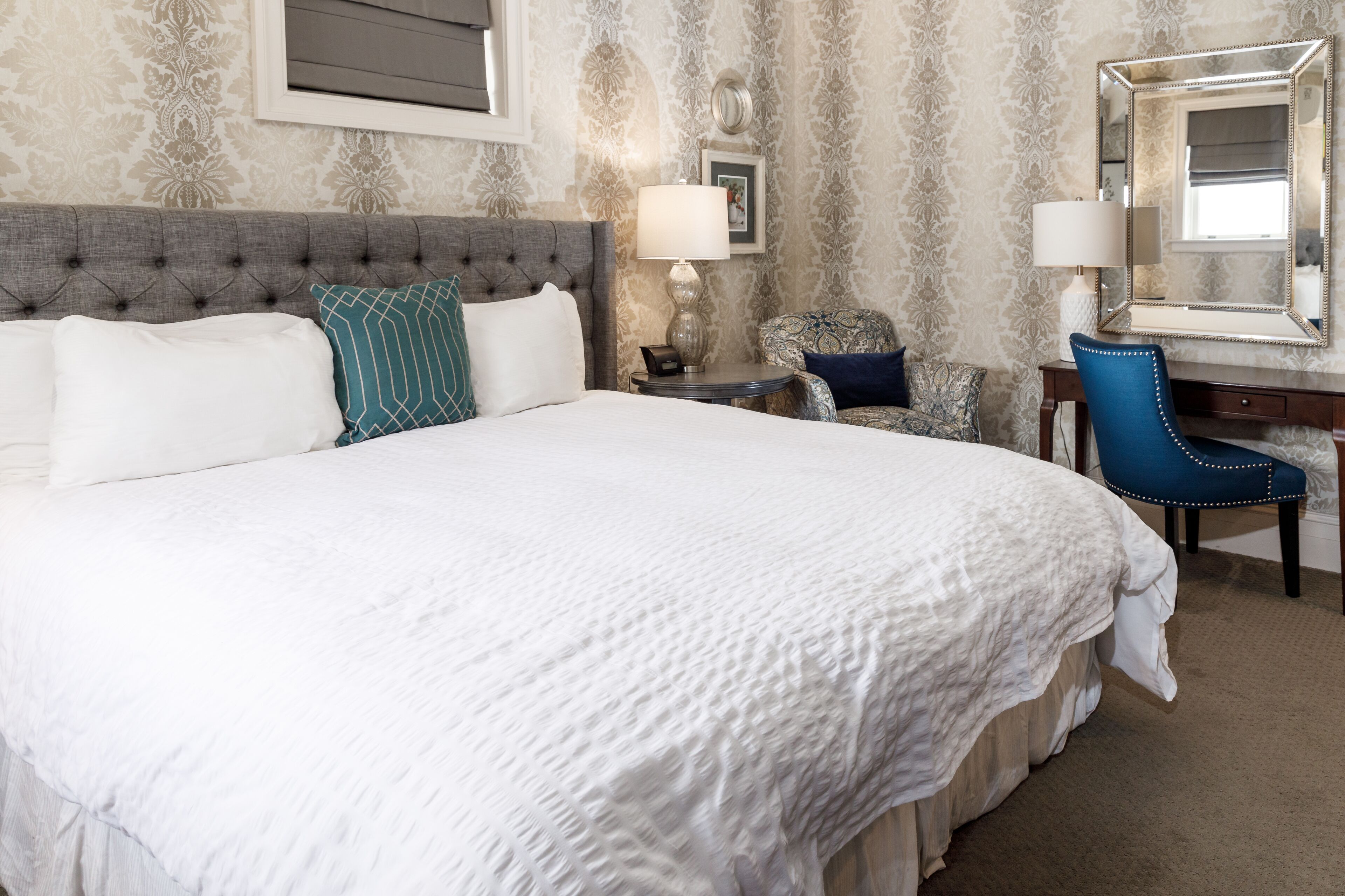 A hotel room with a large bed, a desk, a chair, and a mirror.