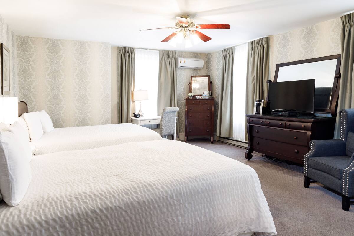 A hotel room with two beds, a dresser, a television, and a ceiling fan.