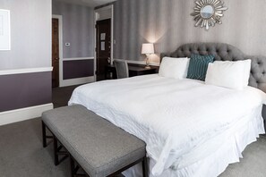 A neatly arranged hotel room with a large bed, a bedside table with a lamp, a chair, and a bench.