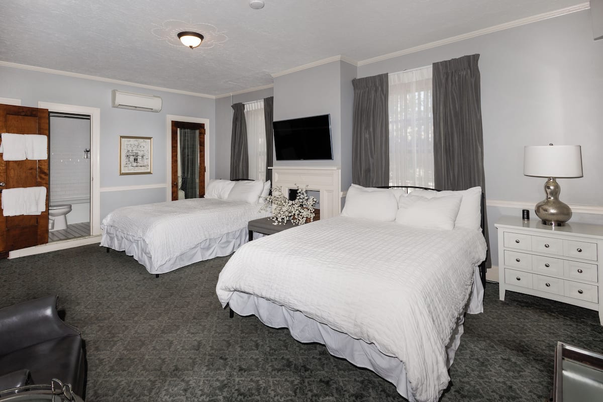 A hotel room with two beds, a TV, a fireplace, a desk, and a chair.
