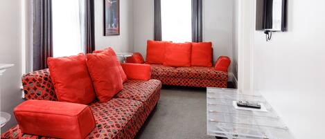 A modern hotel room with a sofa set, a small table, and a TV mounted on the wall.