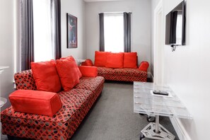 A modern hotel room with a sofa set, a small table, and a TV mounted on the wall.