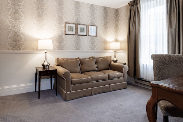 A room with a beige patterned wallpaper, a brown sofa, two side tables with lamps, and a leopard print chair.