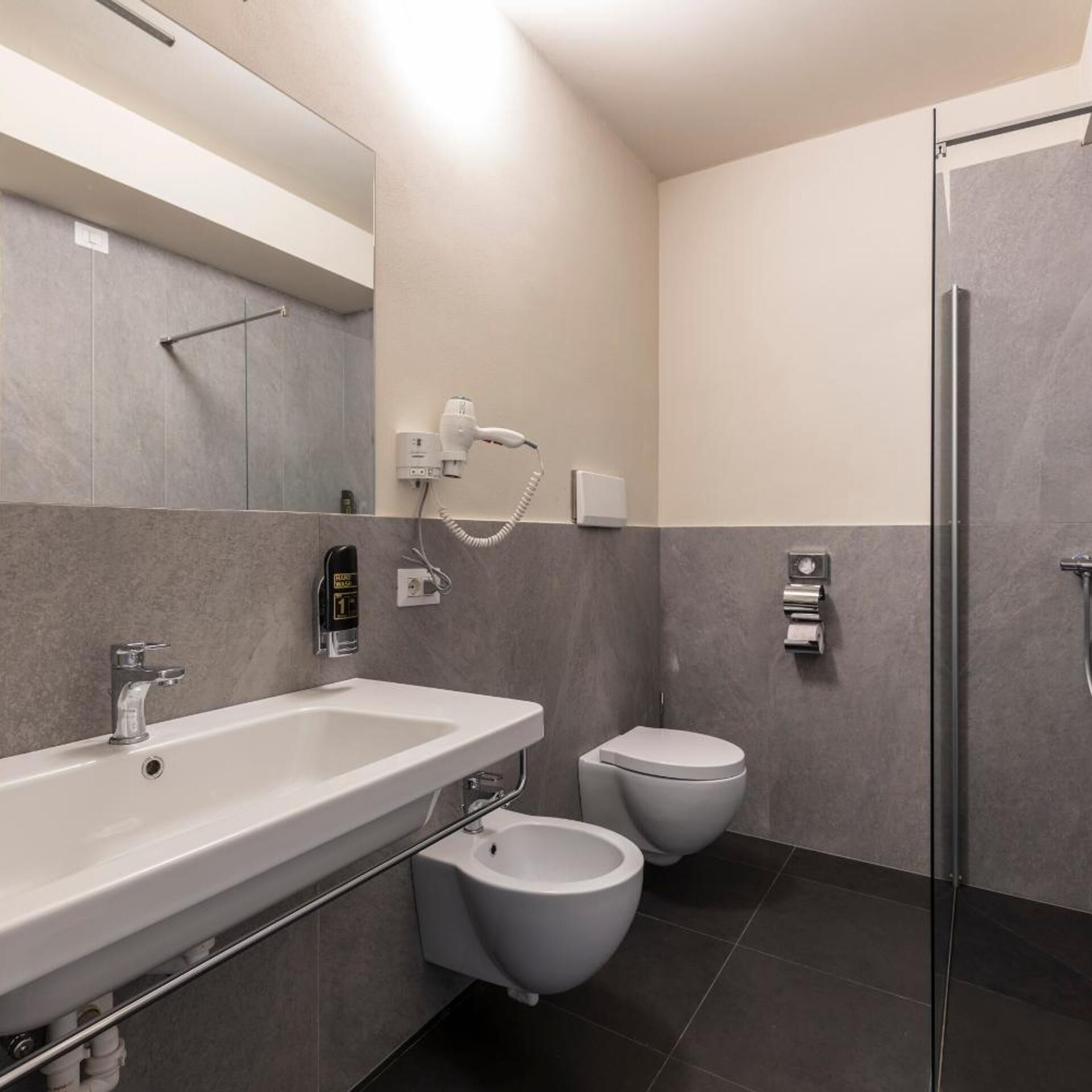 A modern bathroom with a large sink, two toilets, a shower area, and a mirror.