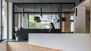 A modern reception desk with a wooden accent, large windows, and hanging pendant lights. - Villa Delle Rose (ARCO)