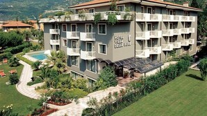 A hotel with multiple balconies, a swimming pool, and a mountainous backdrop. - Villa Delle Rose (ARCO)