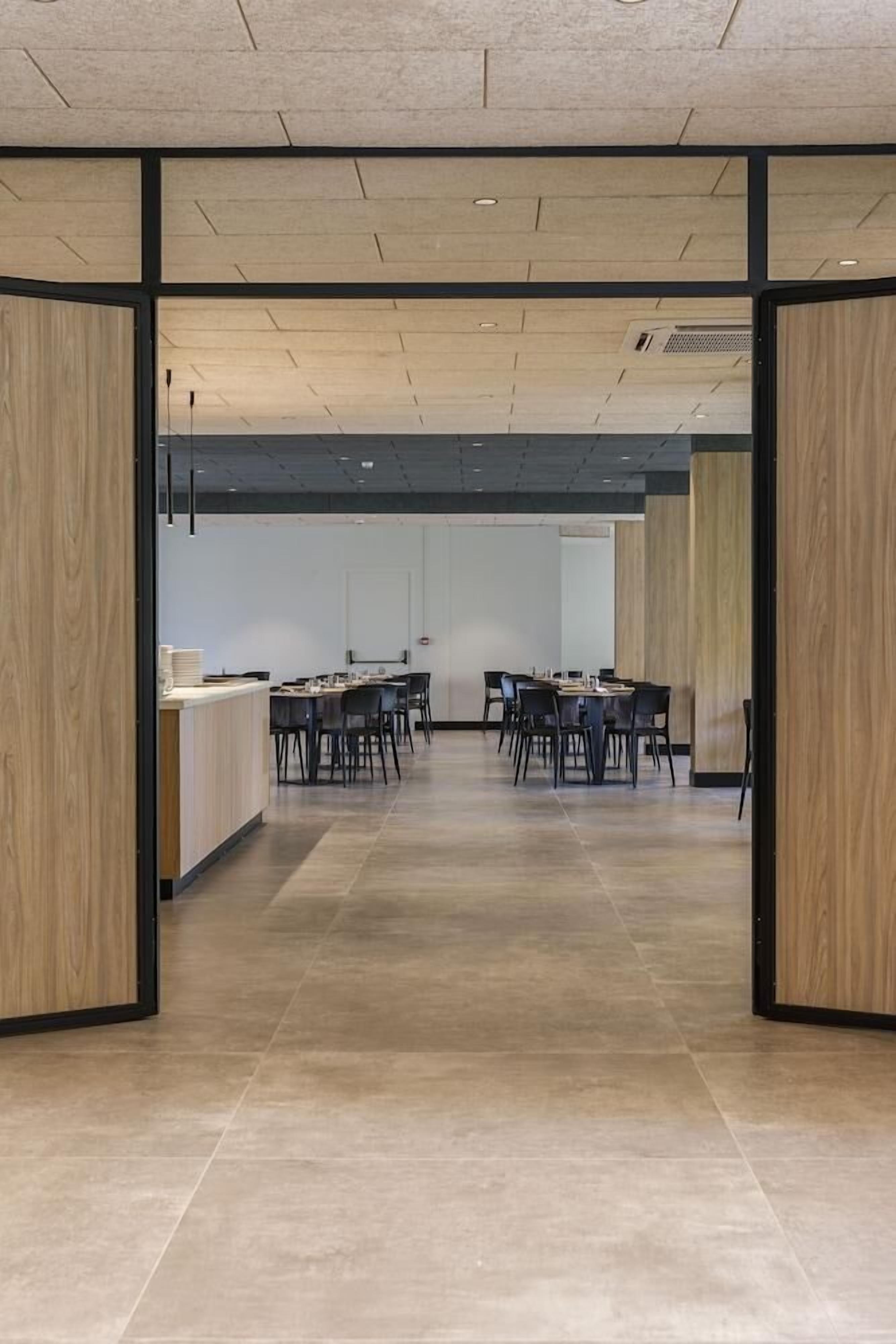 Una sala conferenze moderna con un lungo tavolo e sedie, pareti rivestite in legno e pavimento piastrellato.
