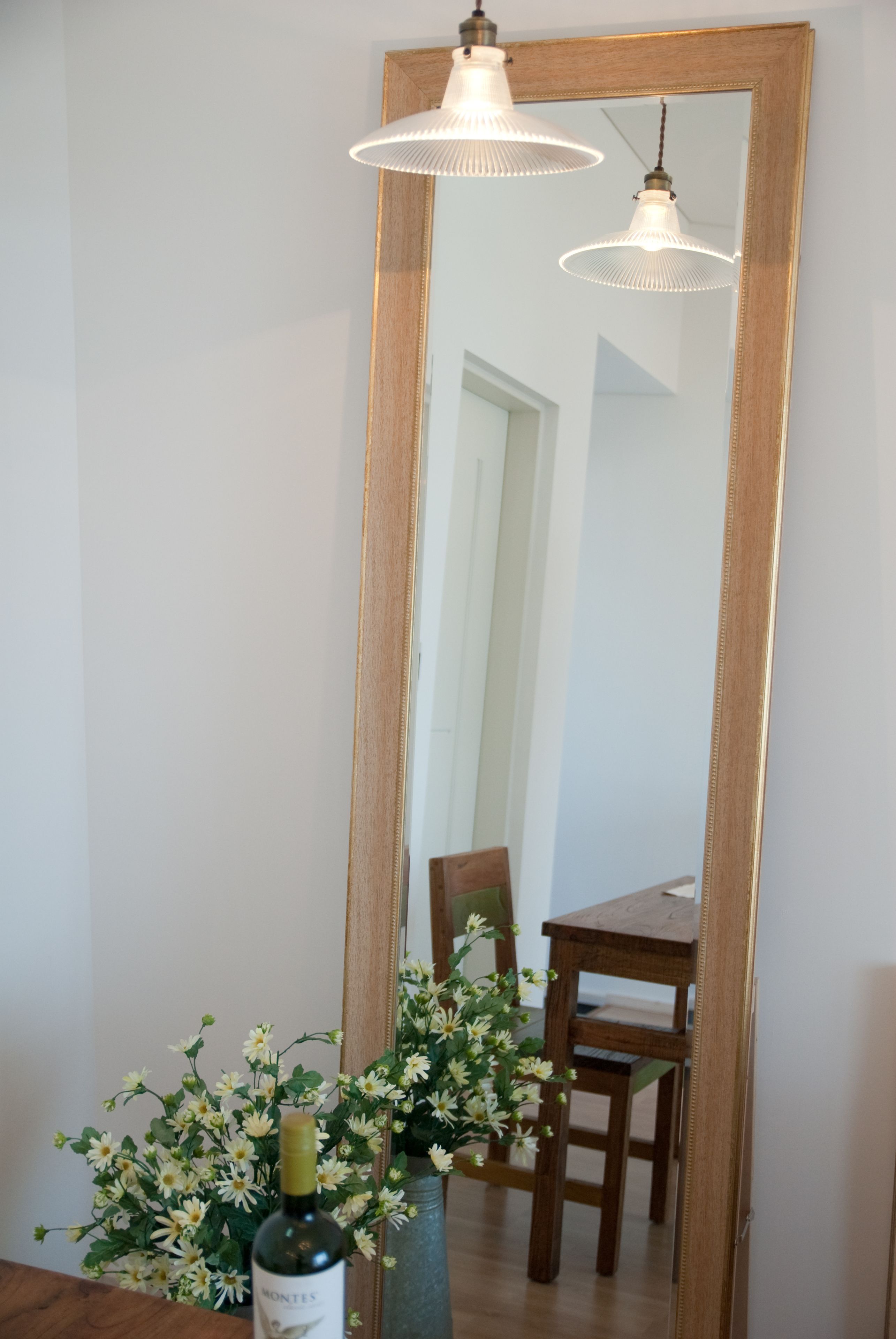A mirror with a wooden frame, a bottle of wine, and a vase of flowers.