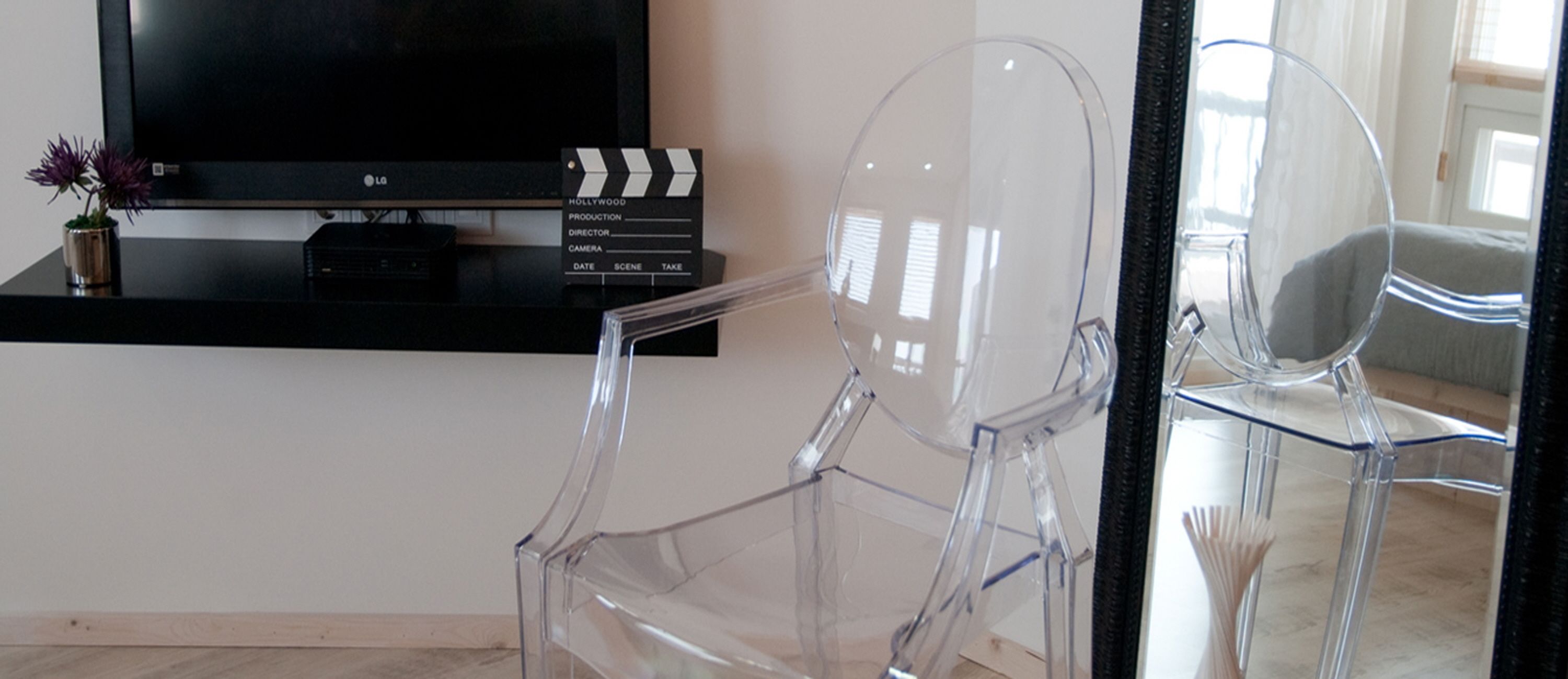 A modern living room with a flat-screen TV, a clapperboard, and a clear glass chair.