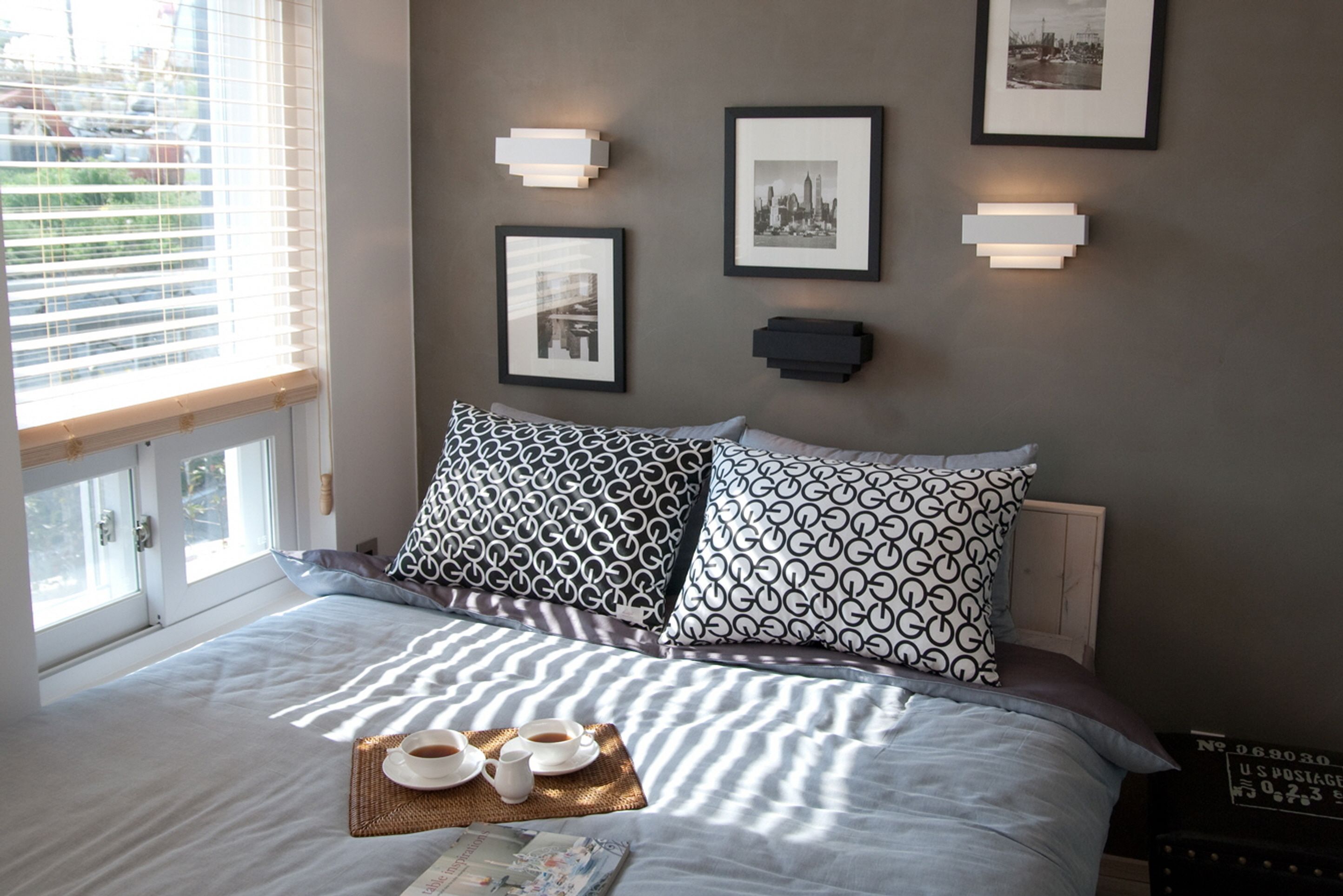A neatly made bed with patterned pillows, a tray with cups and saucers, and framed pictures on the wall.