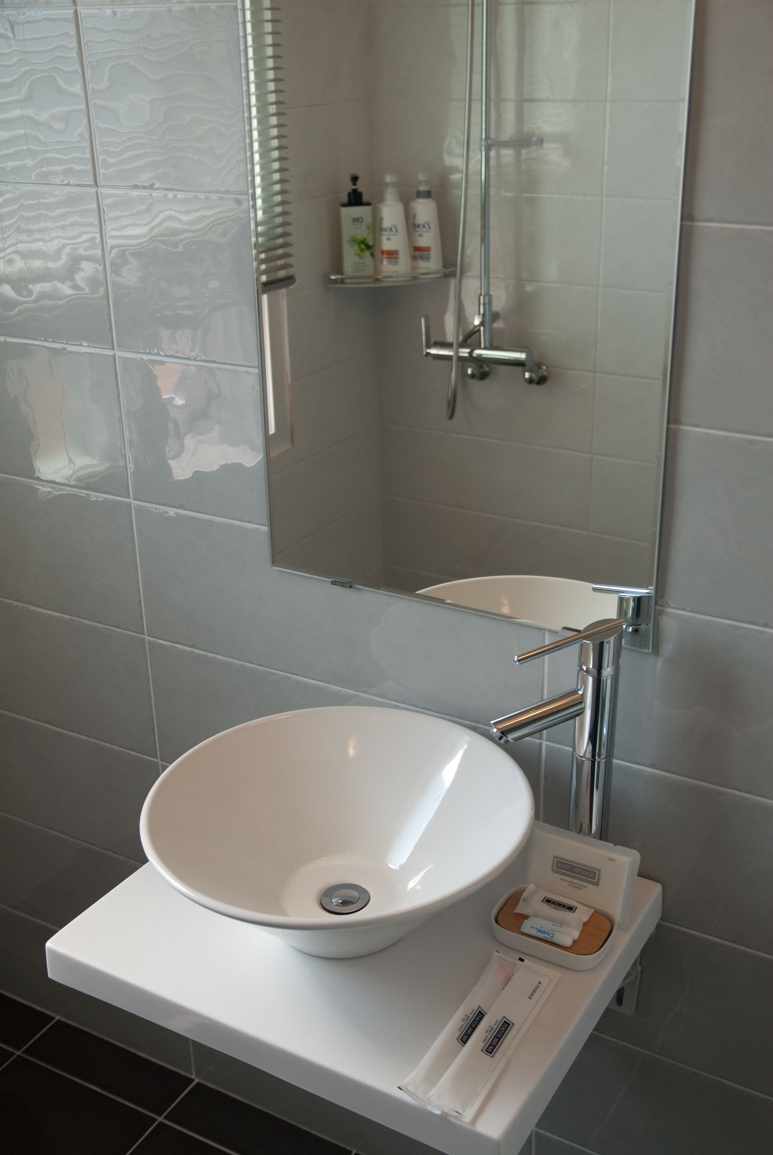 Un baño con un lavamanos blanco tipo recipiente, un espejo y una ducha.