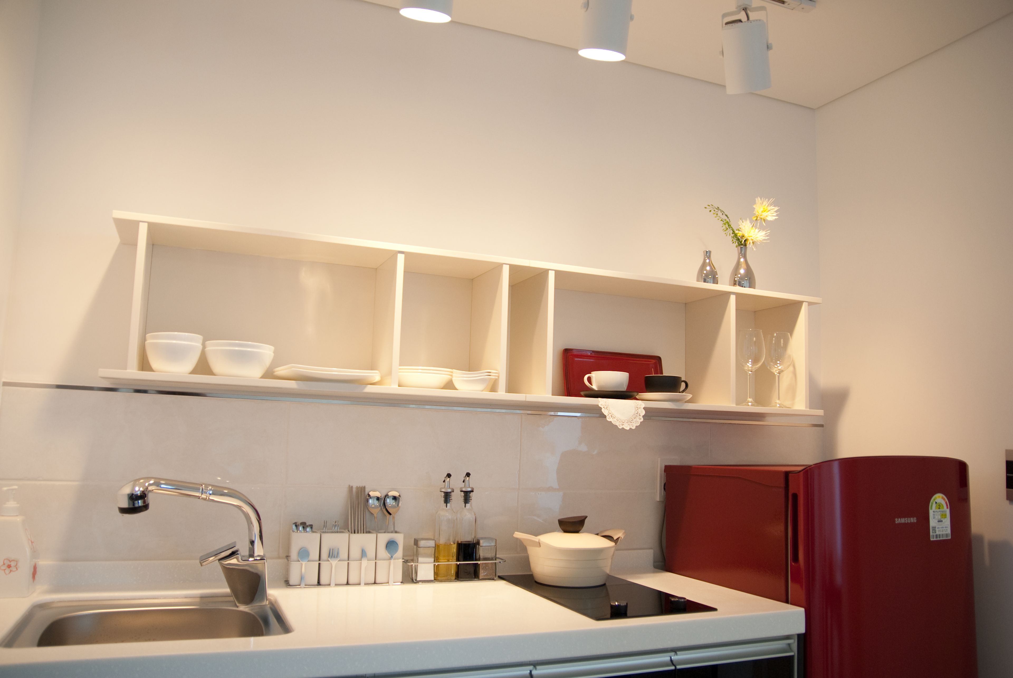 A kitchen with white cabinets, a stainless steel sink, and a red refrigerator.