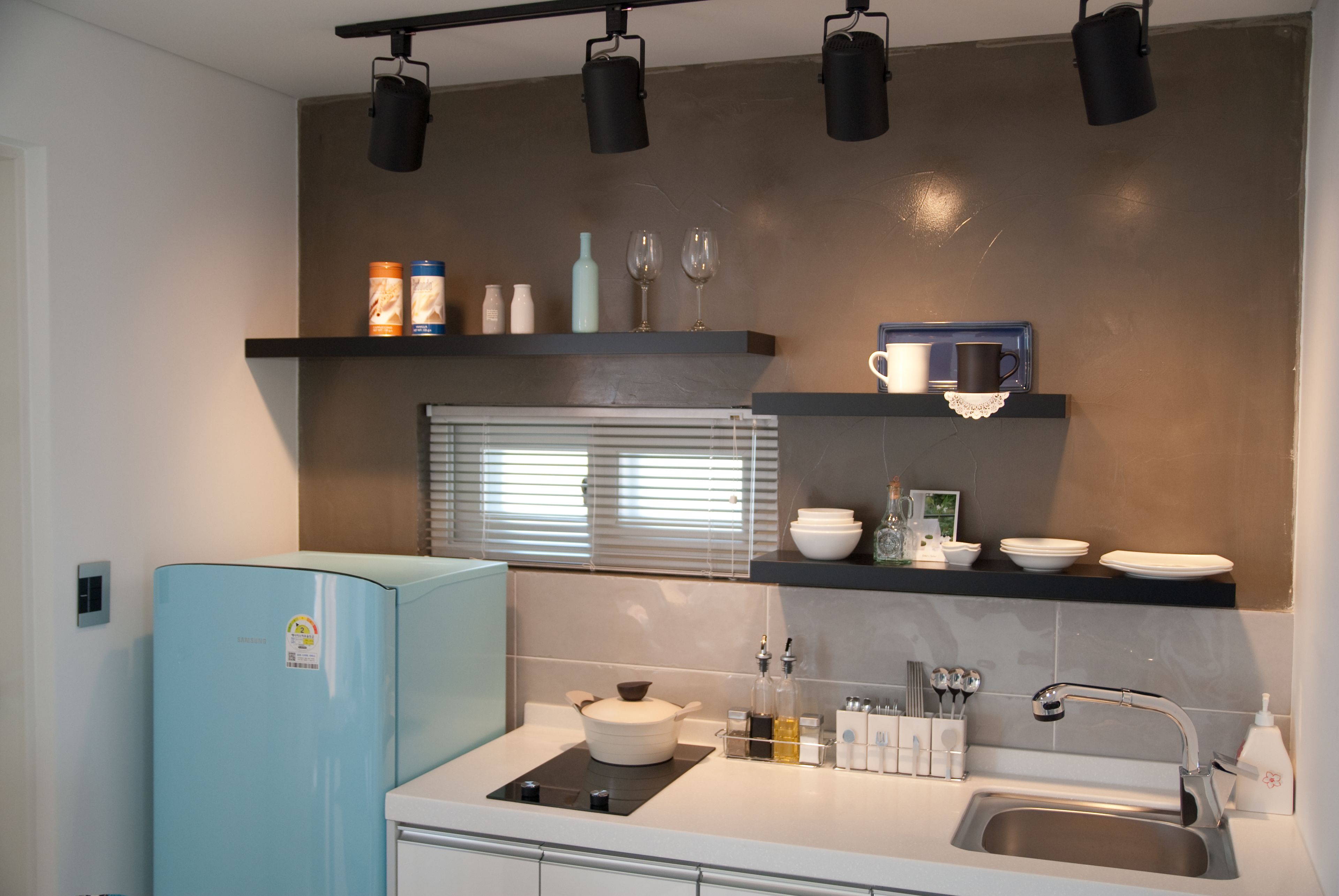A modern kitchen with a light blue refrigerator, a built-in stove, a sink, and overhead lighting.