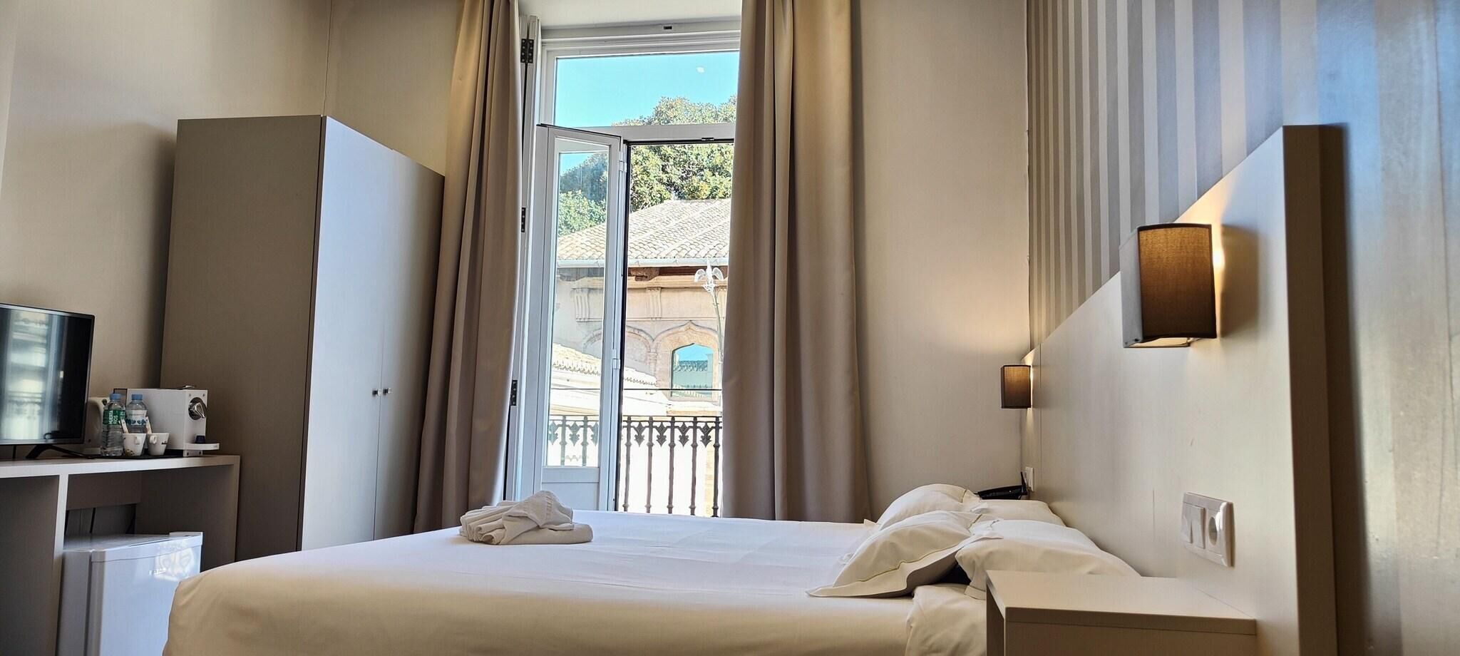 Ein Hotelzimmer mit Bett, Schreibtisch mit Fernseher, Lampe und Blick auf ein Gebäude durch das Fenster.