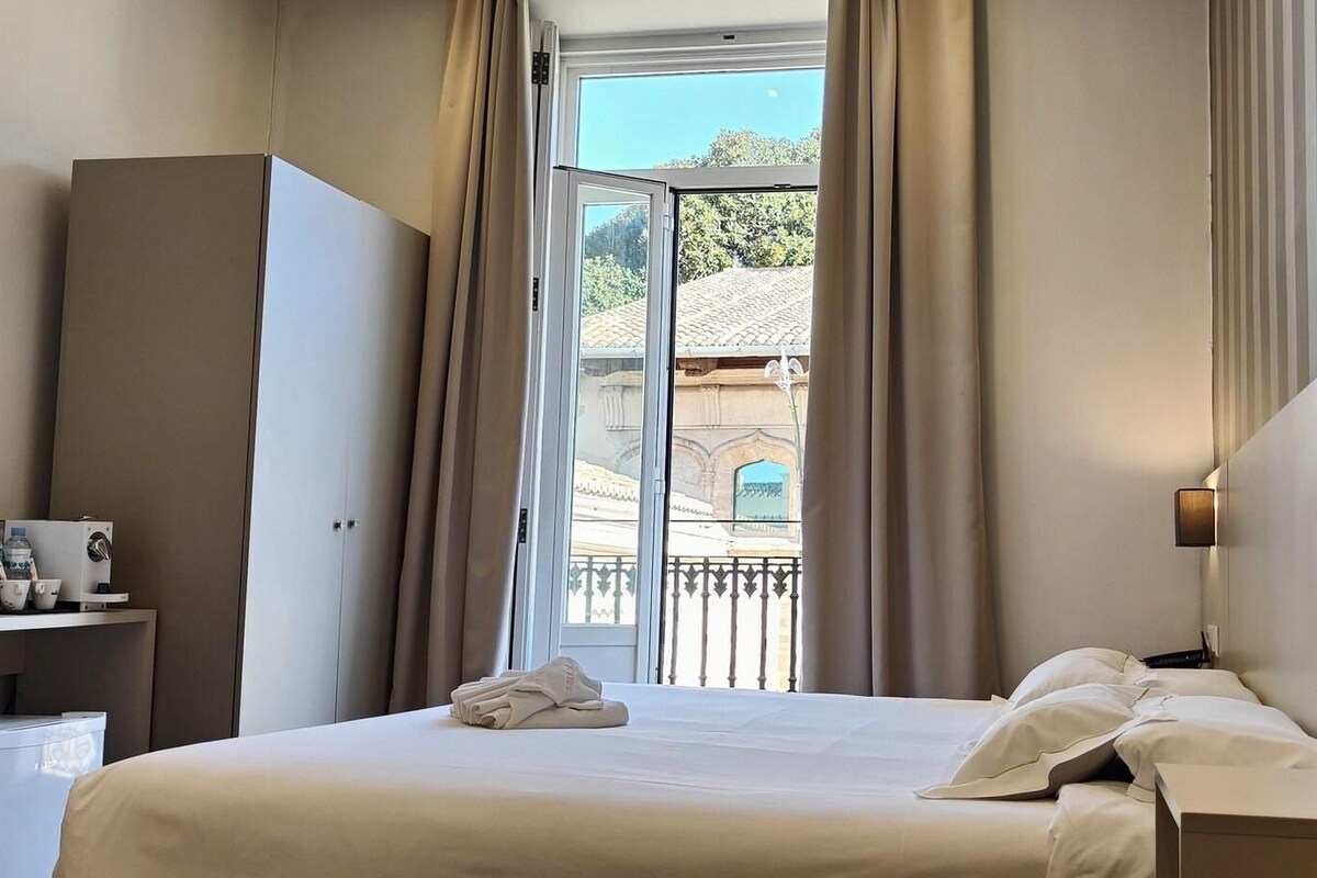 Ein Hotelzimmer mit Bett, Schreibtisch mit Fernseher, Lampe und Blick auf ein Gebäude durch das Fenster.