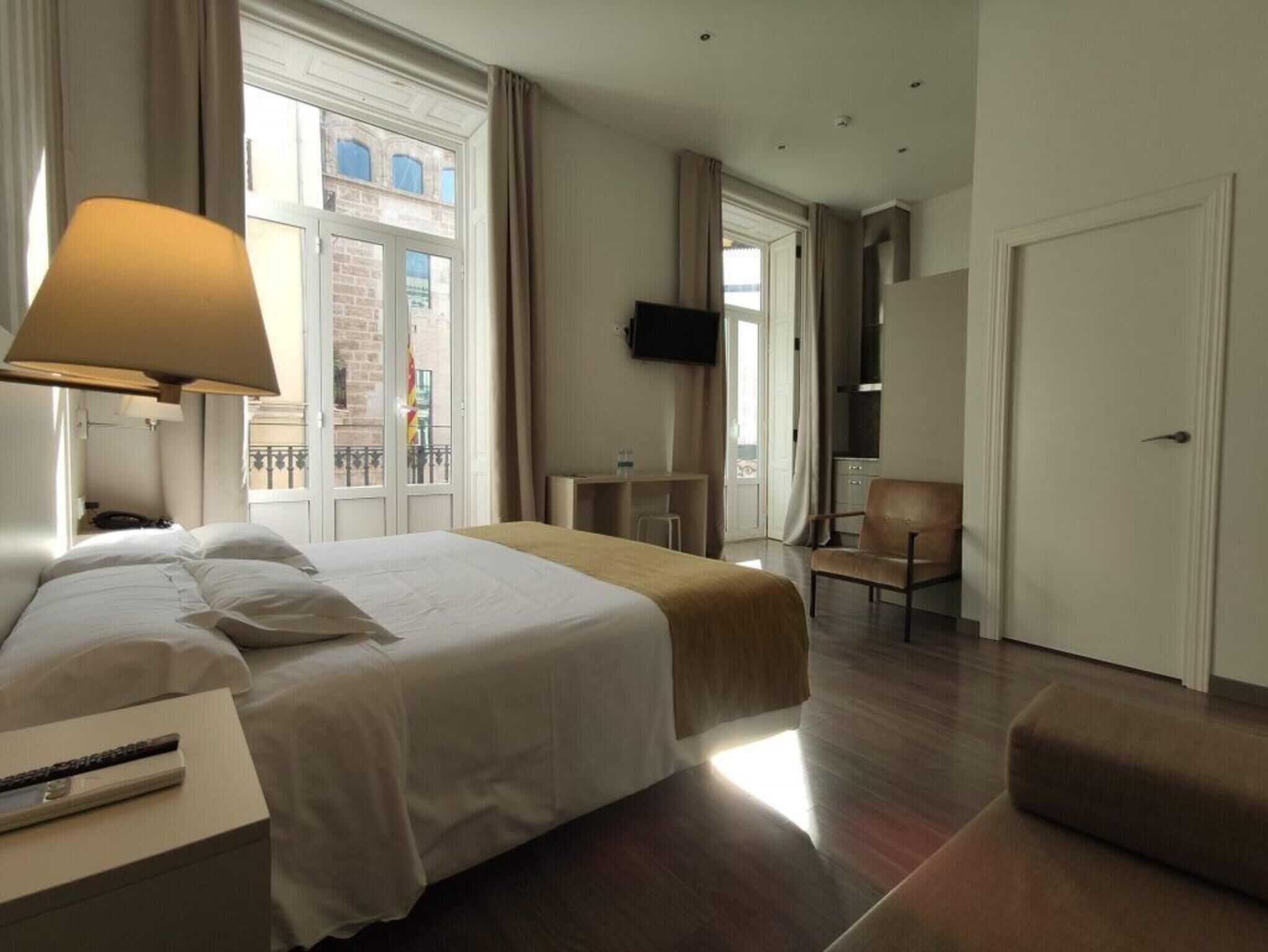Ein Hotelzimmer mit Bett, Nachttisch, Lampe, Fernseher, Stuhl und einer Tür.