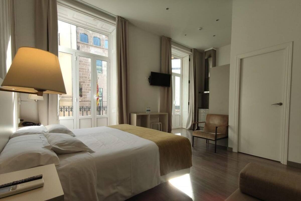 A hotel room with a bed, bedside table, lamp, TV, chair, and a door.