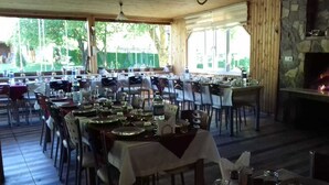 An outdoor dining area with multiple tables set for meals, surrounded by chairs, and a stone fireplace in the background. - Abant Hayalim Pansiyon (Bolu)