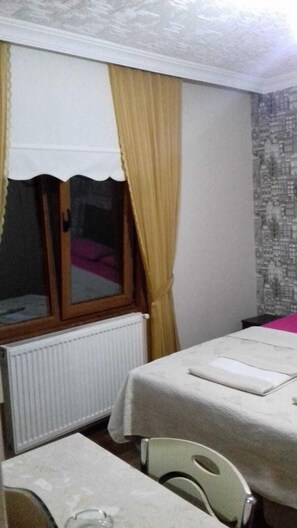 A hotel room with a bed, a window with curtains, a radiator, and a chair. - Abant Hayalim Pansiyon (Bolu)