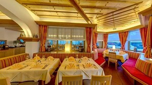 A restaurant with tables set for dining, a bar area, and a view of the sea. - Almhotel Karnten (Hermagor-Pressegger See)
