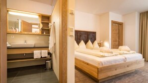 Hotellihuone, jossa on puinen sänky, suuri peili, pesuallas ja pieni roskakori.