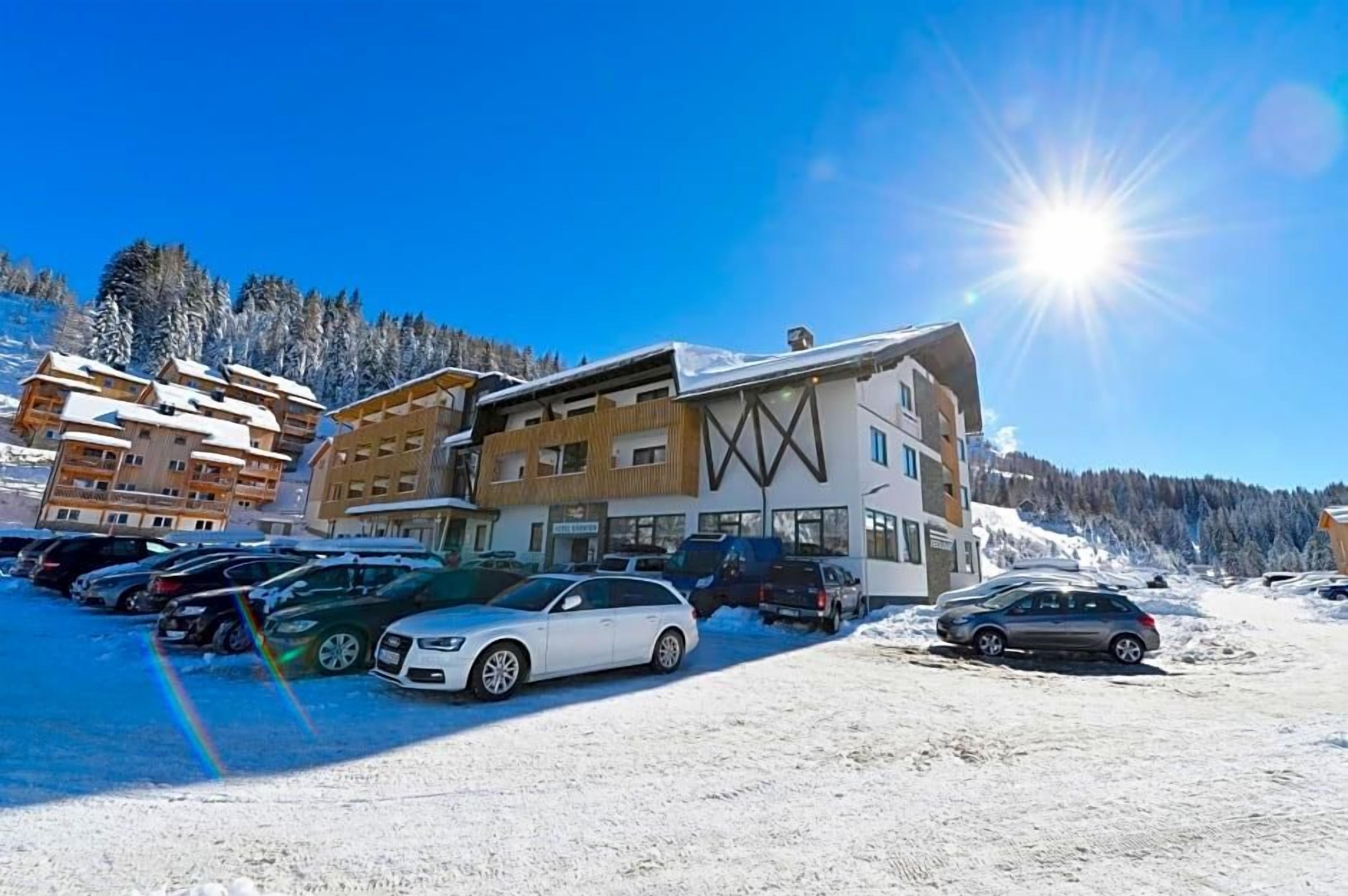 A modern building with a ski resort backdrop, featuring a parking lot with several cars.