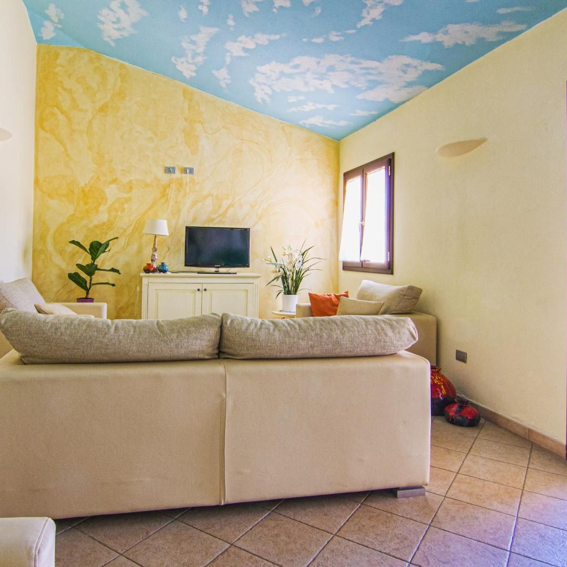 Ein Wohnzimmer mit Sofa, Fernseher und Zierpflanzen.