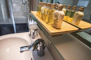 A bathroom with a wooden shelf holding various bottles of Pure Herbs shampoo and conditioner. - La Perla (Tortoli)