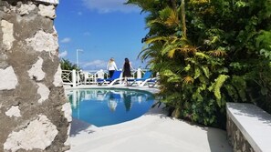 A pool area with two people walking near the edge, surrounded by lush greenery and a white wall. - Tranquility Villa (Port Antonio)