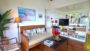 A cozy living room with a sofa, a coffee table, a TV, and a bookshelf filled with decorative items. - Tranquility Villa (Port Antonio)