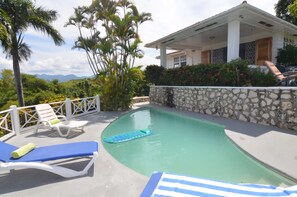 A pool area with lounge chairs, a stone wall, and a view of mountains. - Tranquility Villa (Port Antonio)