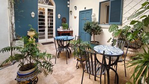 A courtyard with a dining table and chairs, potted plants, a blue door, and a white wall with a window. - Julina Boutique Living (Mosta)