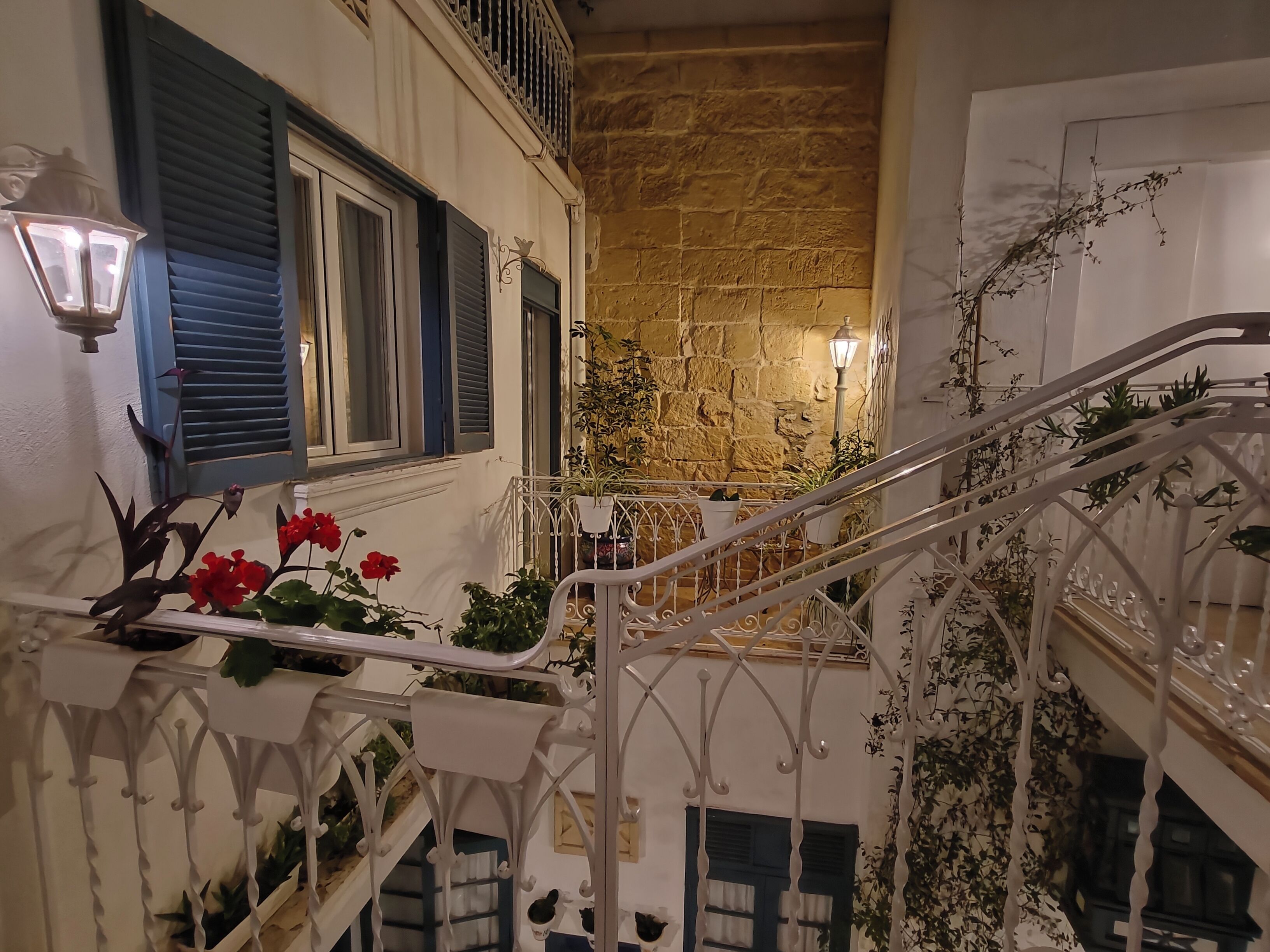 A staircase with white railings, blue shutters, and potted plants.