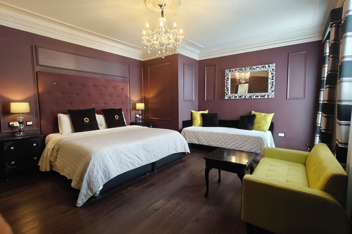 A hotel room with two beds, a chandelier, a mirror, and a yellow armchair.