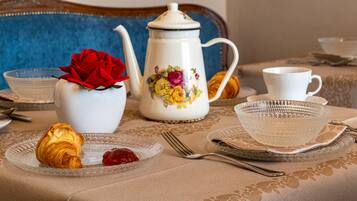 A dining table with a floral teapot, a croissant, and a glass bowl.