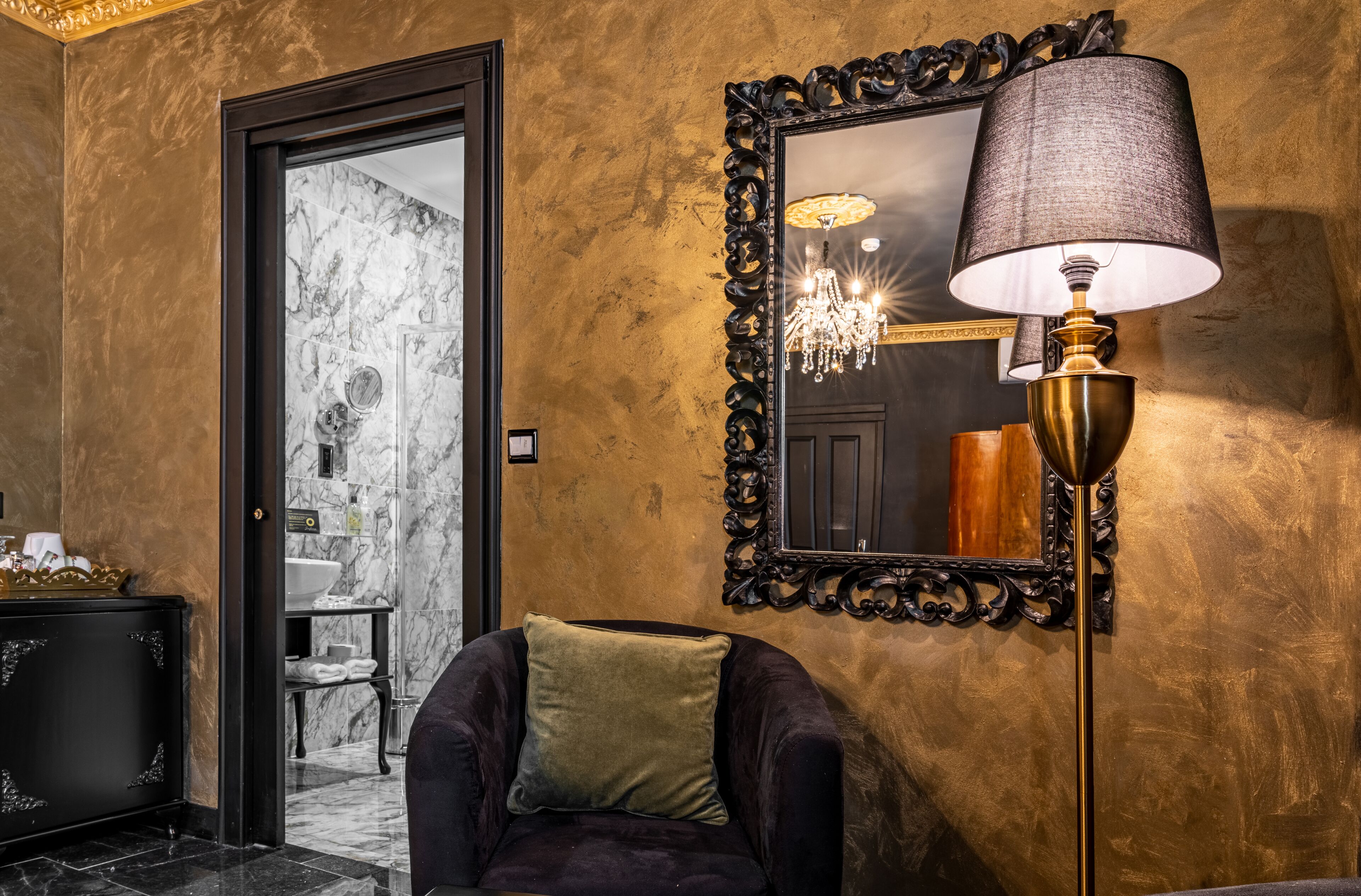 Een luxueuze kamer met een marmeren wand, een grote spiegel, een comfortabele fauteuil en een vloerlamp.
