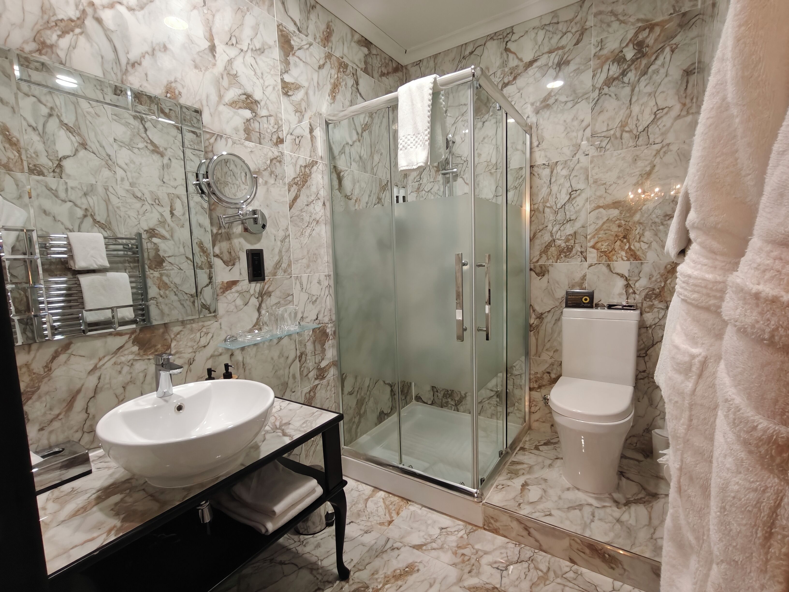 Un baño moderno con salpicadero de mármol, ducha con cerramiento de vidrio, lavabo blanco y un inodoro.