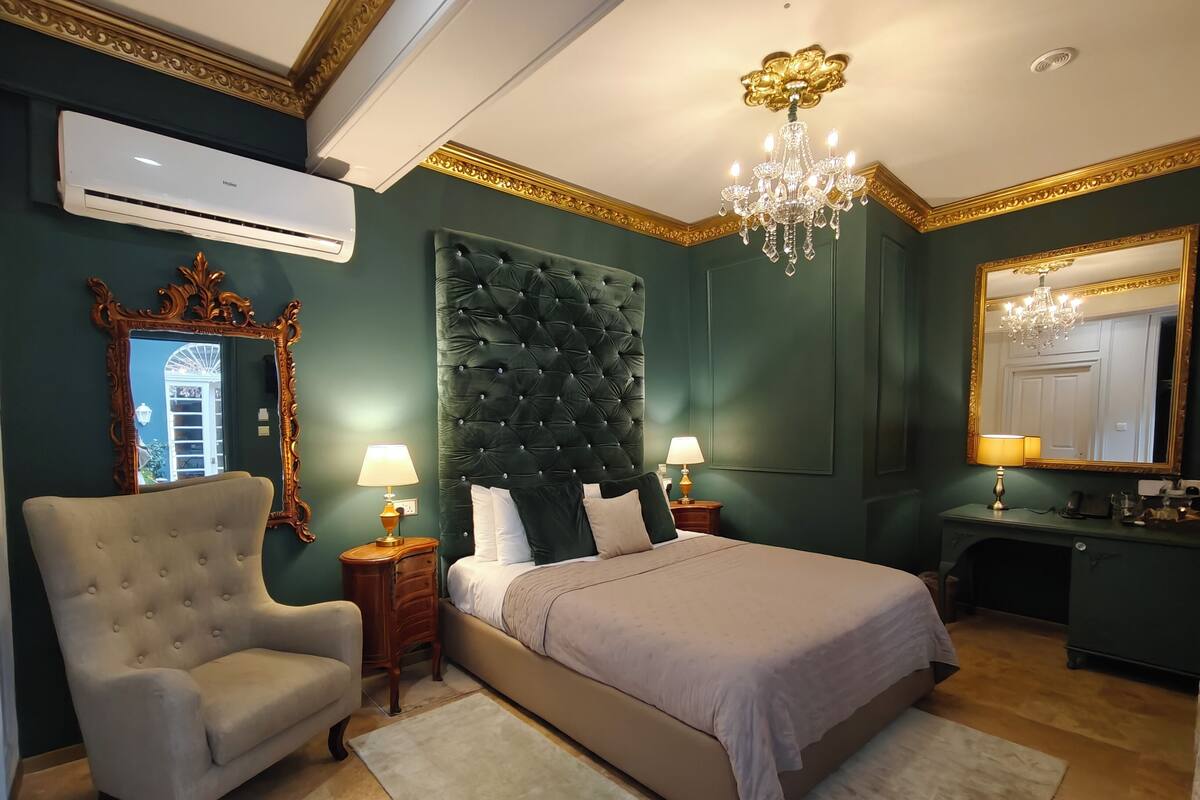 A bedroom with a tufted headboard, two bedside lamps, a large mirror, and a chandelier.