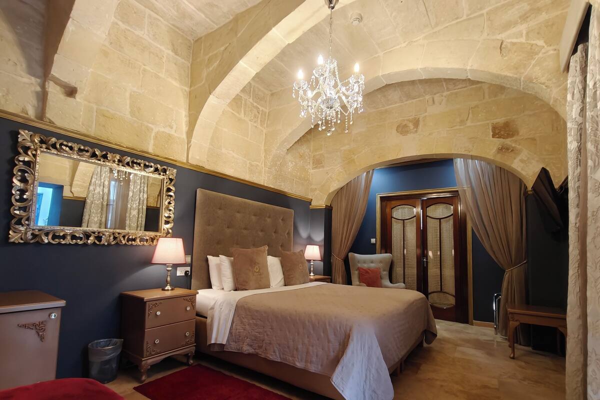 A bedroom with a large bed, a chandelier, a mirror, and a wardrobe.
