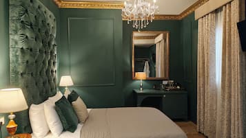 A bedroom with a tufted headboard, a chandelier, a bedside table with a lamp, a dresser, and a mirror.