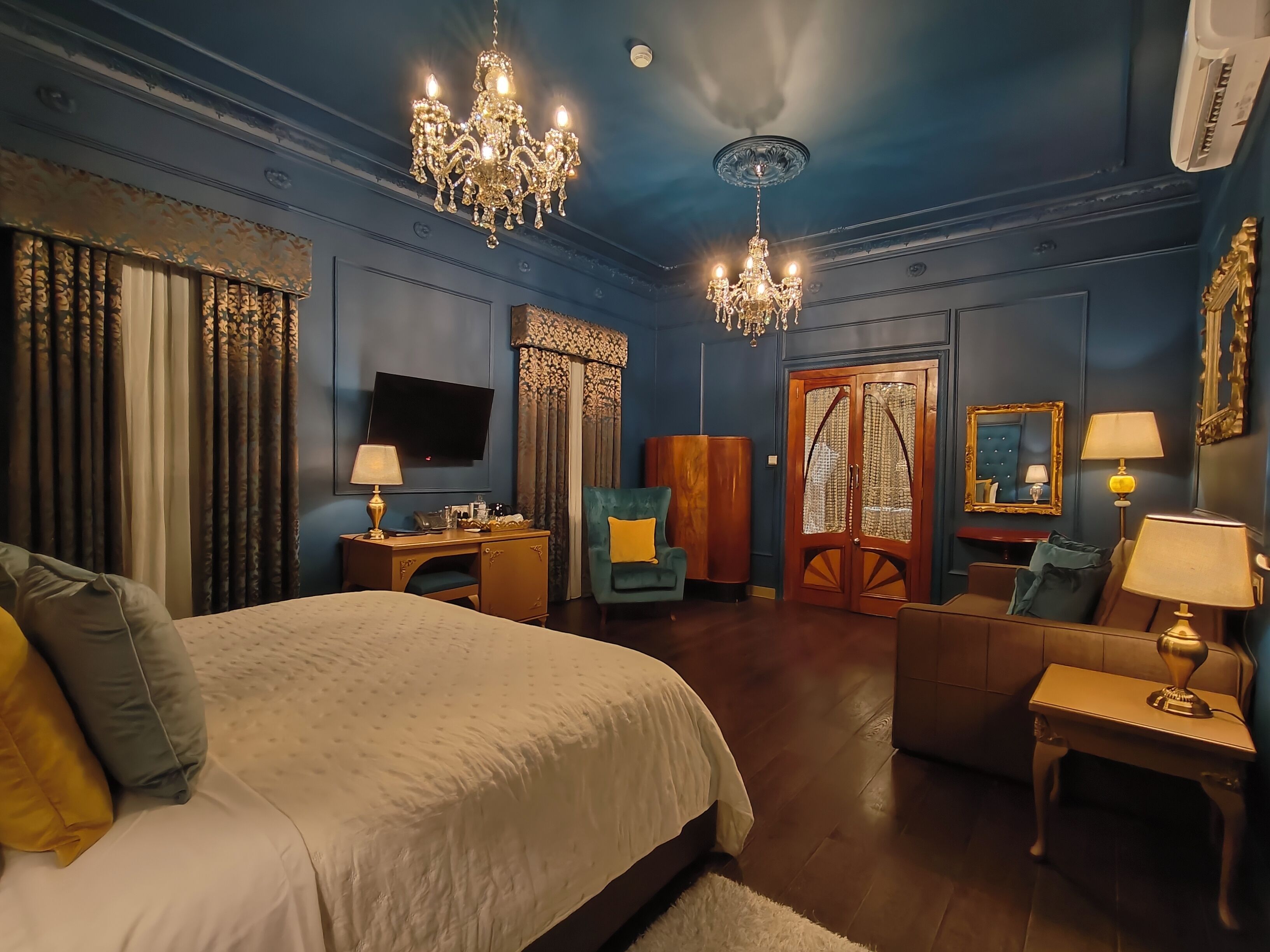 Una habitación de hotel con una cama grande, un escritorio, un televisor, una araña y un armario de madera.