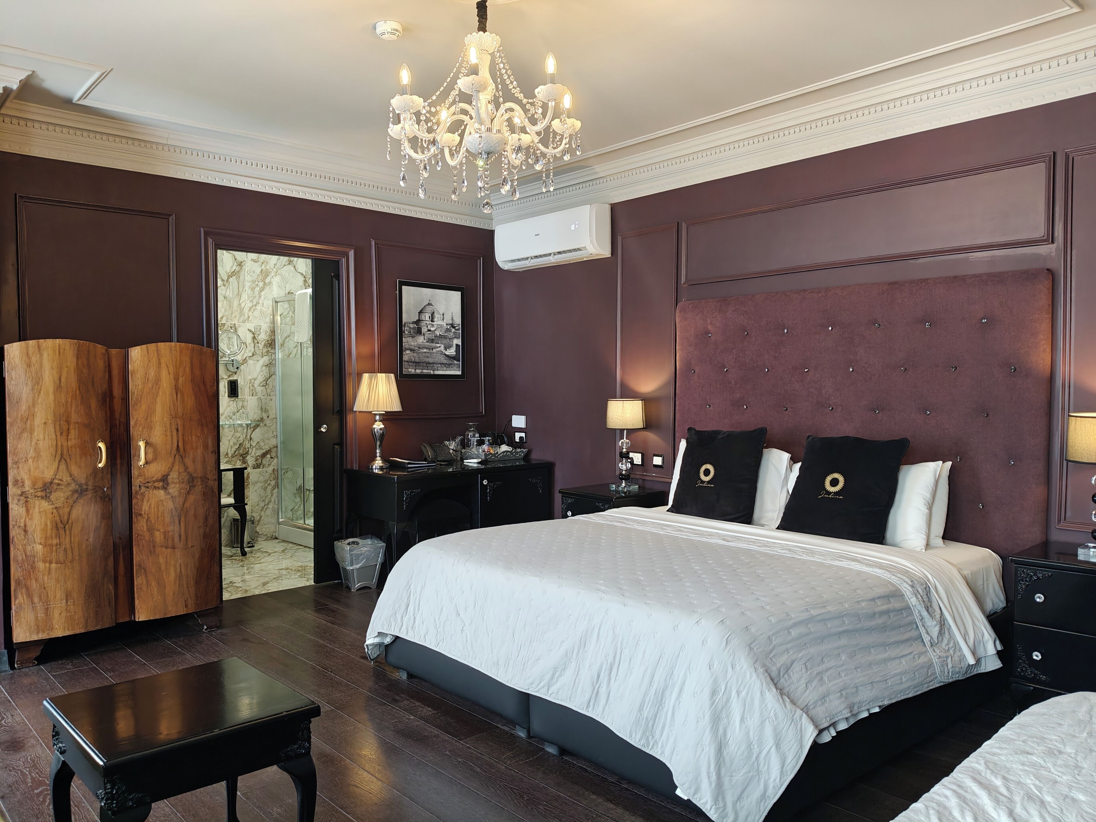 A bedroom with a large bed, a chandelier, a wardrobe, and a nightstand with lamps.