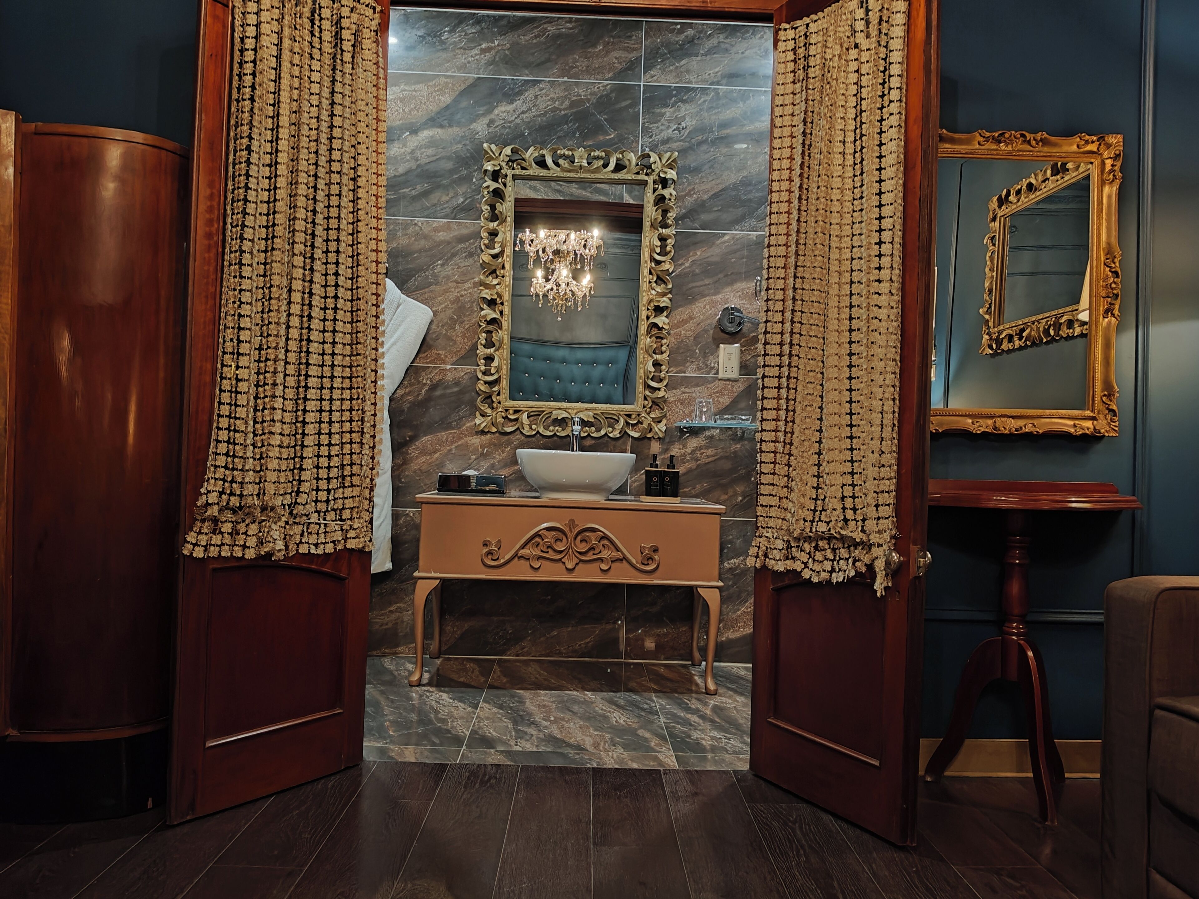 Un baño con pared de mármol, un espejo grande, tocador con lavabo y puerta de madera.