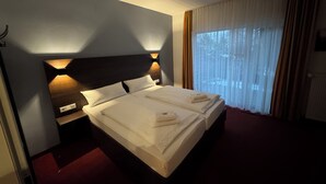 A hotel room with a large bed, a nightstand, a wall-mounted light, and a window with curtains. - Altes Doktorhaus (Willingen)
