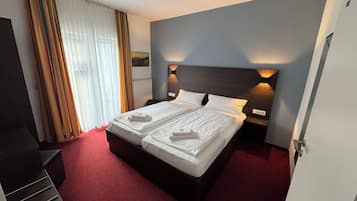 Habitación de hotel con una cama grande, dos mesitas de noche, una alfombra roja y una ventana con cortinas.