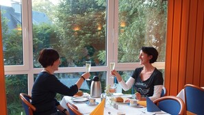 Two people seated at a table with a view of greenery outside. - Altes Doktorhaus (Willingen)