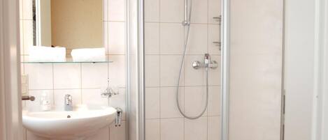 A bathroom with a glass-enclosed shower, a sink, a toilet, and a small stool.