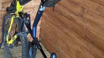 Een fiets leunt tegen een houten muur in een kamer met een schuine plafond.