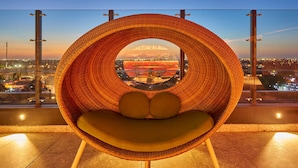 A wicker chair with a circular window view of a cityscape at dusk. - City Express Plus by Marriott Mérida (Mérida)
